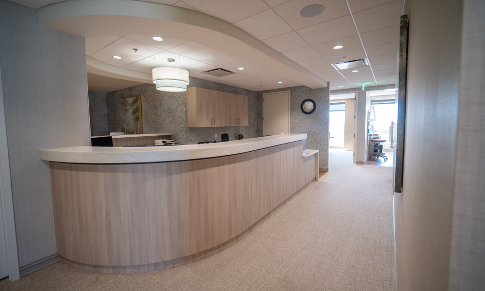 Modern dental office front desk with curved wood-paneled reception counter, overhead pendant lighting, and hallway leading to treatment rooms