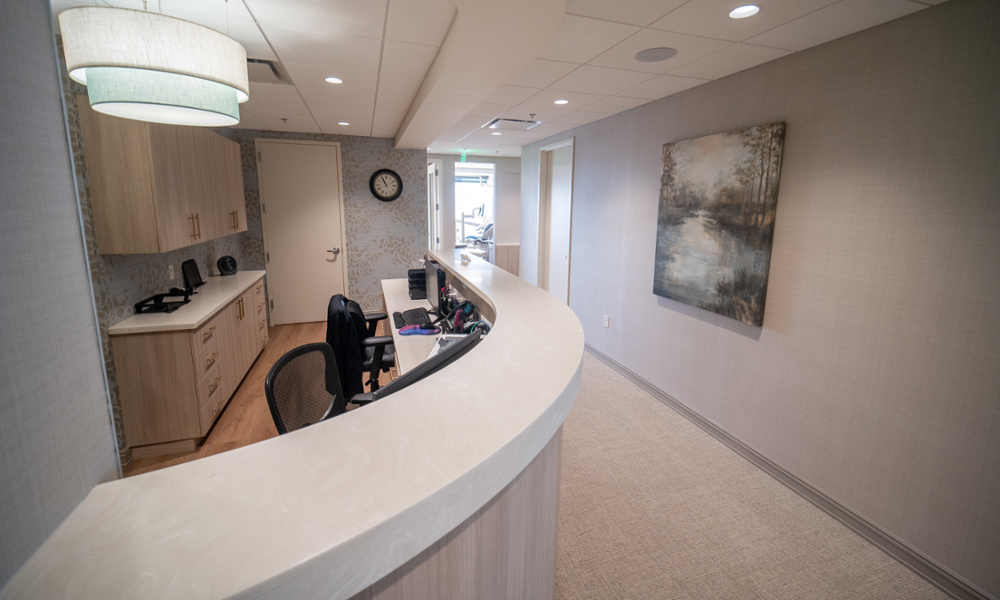 Modern dental office reception desk with curved white counter, wood cabinetry, and elegant pendant lighting